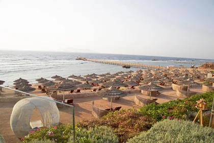 Rows of straw parasols on the beach with the pier reaching into the Red Sea