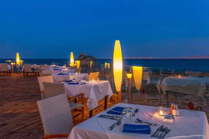 Candlelit dinner tables laid beside the sea at dusk